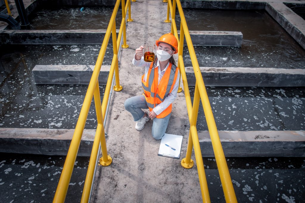 female worker takes a water sample in in a wastewater treatment plant where regular facility safety inspections are recommended